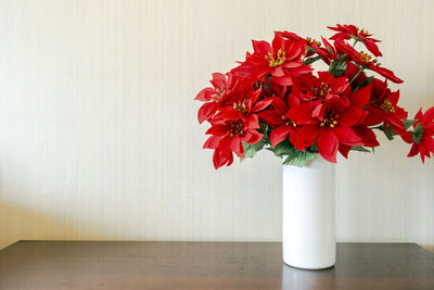 Close-up of red flower vase on table against wall