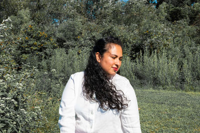 Young woman looking down while standing against trees