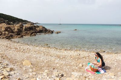Woman sitting on rock by sea against sky