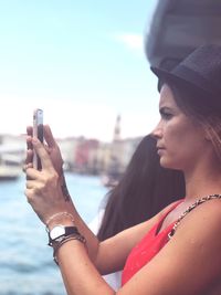 Young woman looking away while photographing on mobile phone by canal