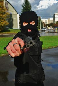 Portrait of burglar in mask aiming gun on street