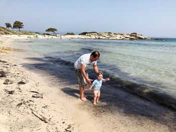 Father and son walking at sea shore against clear sky