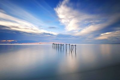 Wooden posts in sea against sky at sunset