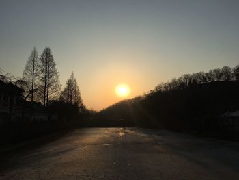 Road amidst silhouette trees against sky during sunset