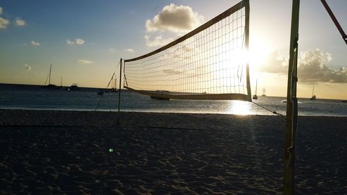 Net at beach against sky during sunset