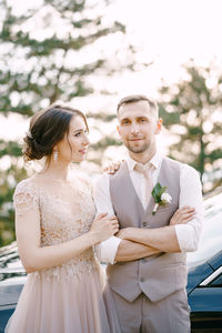 Portrait of bride and bridegroom standing against trees