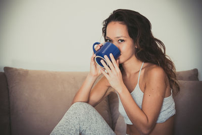 Portrait of young woman using phone while sitting on sofa at home