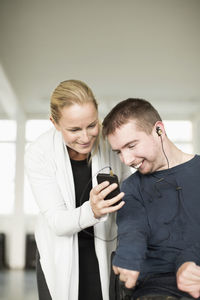 Female caretaker assisting disabled man in using mobile phone at home