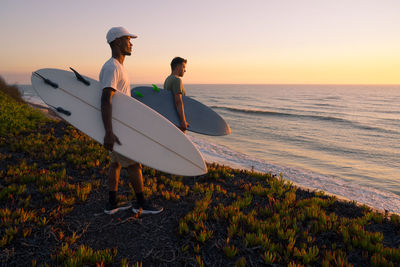 Rear view of woman standing on beach against sky during sunset