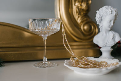 A glass glass with pearl beads near a plate and a plaster figure