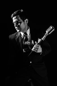 Young man holding microphone against black background