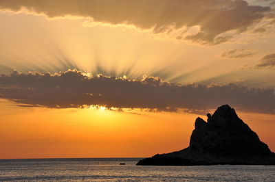 Scenic view of silhouette rock in sea against sky during sunset