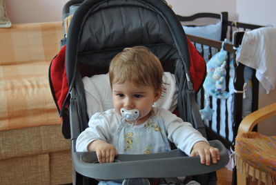 Cute baby boy sucking pacifier in stroller at home