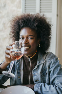Portrait of smiling young woman with afro hairstyle drinking wine at patio