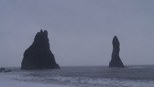 Silhouette rock in sea against clear sky