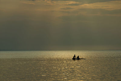 Silhouette people on sea against sky during sunset