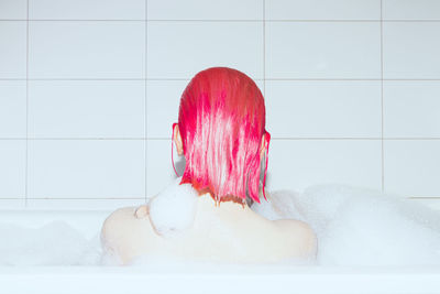 Girl with pink hair takes a bubble bath. self care. back view.
