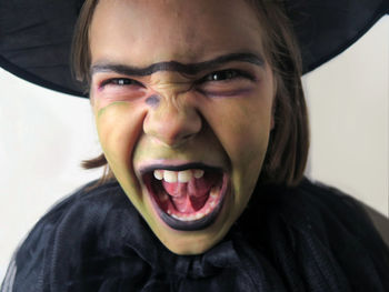 Close-up portrait of girl wearing witch costume and hat standing with mouth open against wall at halloween