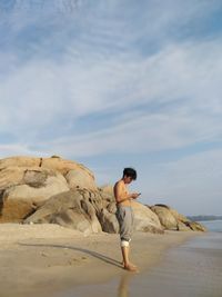 Man standing on rock at beach against sky