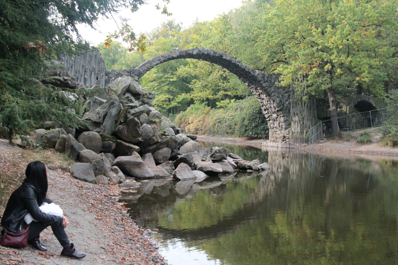 LOW SECTION OF WOMAN SITTING ON ROCK BY RIVER