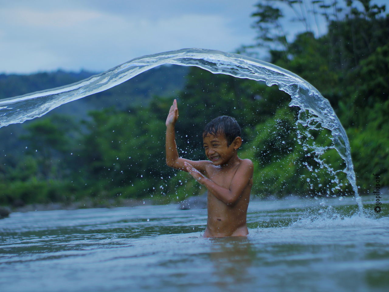 FULL LENGTH OF SHIRTLESS BOY SPLASHING WATER IN WATERFALL