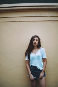 Portrait of young woman standing against wall