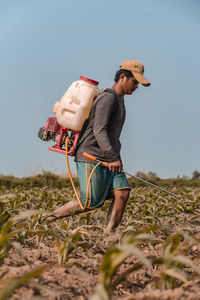Farmer spraying pesticide on agricultural field against clear sky