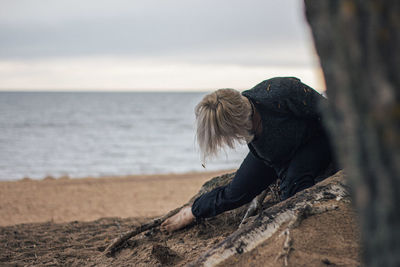 Young woman relaxing on sand at beach against sky