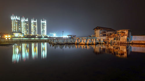 Illuminated buildings by river against sky at night