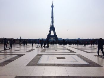 People walking in front of eiffel tower against sky during sunny day