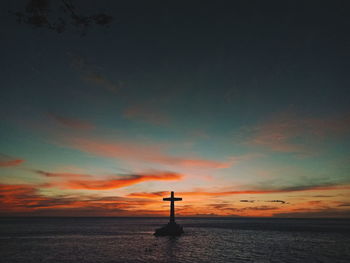 Cross on beach against sky during sunset