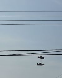 Low angle view of shoes hanging on cables against sky