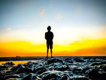 Silhouette man looking at sea against sky during sunset