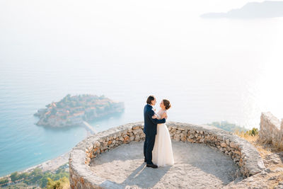 Couple standing on sea shore against sky