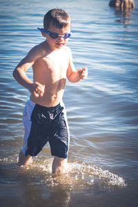 Cute shirtless boy walking on shore at beach