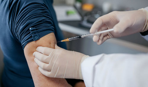 Cropped hand of doctor injecting syringe in patients arm