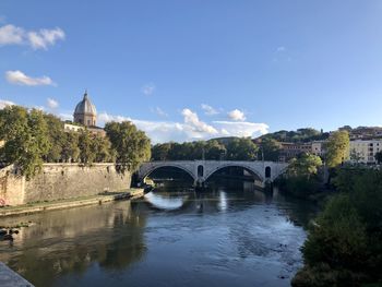 Arch bridge over river by buildings against sky, rome