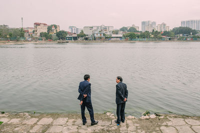 Rear view of men standing on shore against city