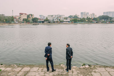 Rear view of business person standing on riverbank against city