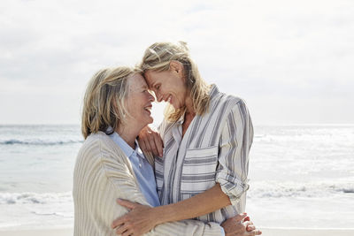 Senior woman and her adult daughter standing on the beach, embracing