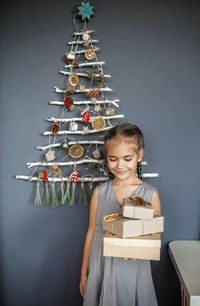 Smiling girl holding gift against christmas tree hanging on wall