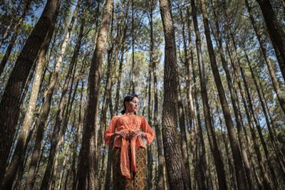 Low angle view of young woman standing at forest