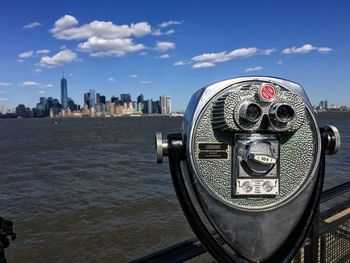 Close-up of coin-operated binoculars by river against cityscape