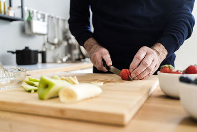 Senior man cutting strawberry on cutting board in kitchen