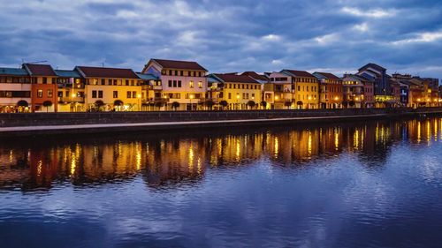 Buildings by lake against sky at dusk