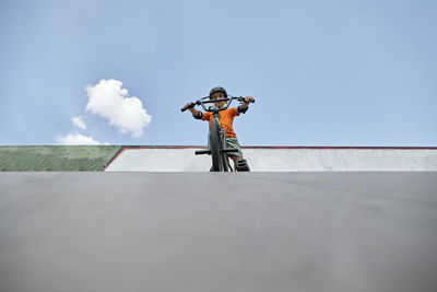 Boy with bmx bike at skateboard park in front of sky