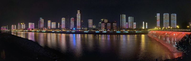 Illuminated buildings by river against sky at night