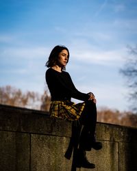 Side view of young woman sitting against the wall