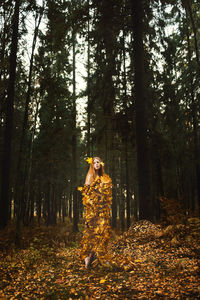 Young woman covered with leaves standing at forest during autumn