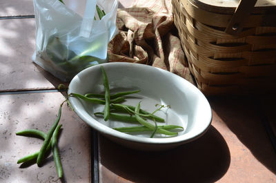 High angle view of green beans by wicker basket on table